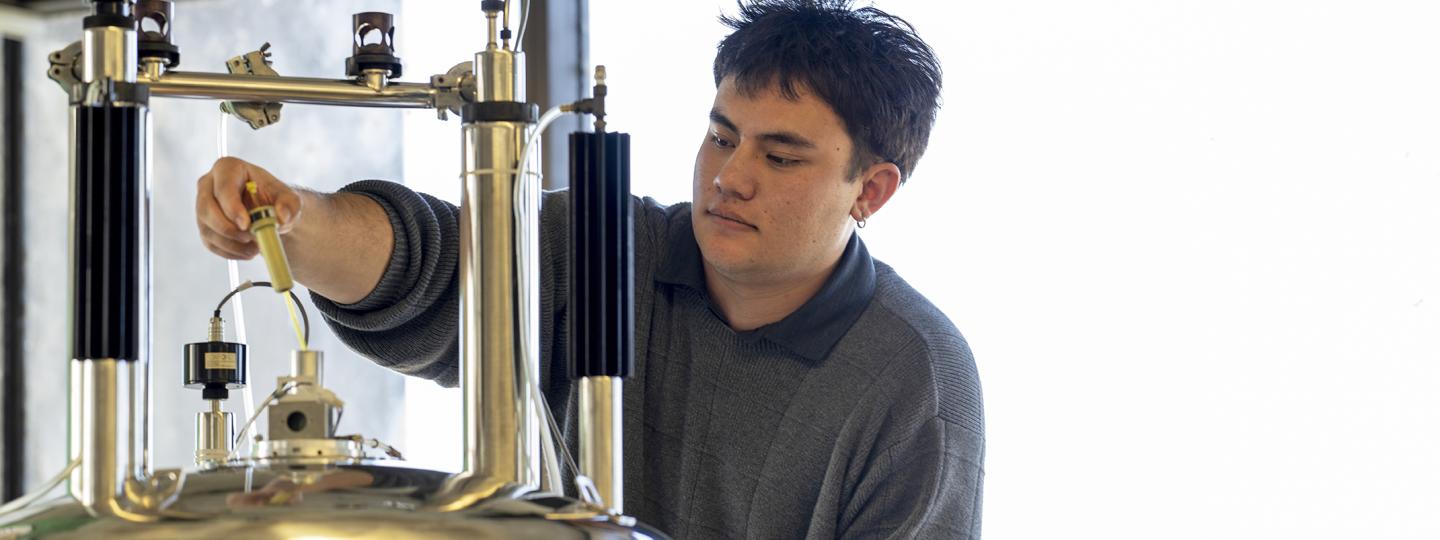 A person concentrates while inserting a tool into the top of a large cylindrical machine.
