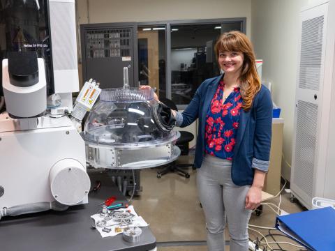Valerie Brogden poses next to the the Noble Dome, a transparent dome with gloves attached, connected directly to a microscope.